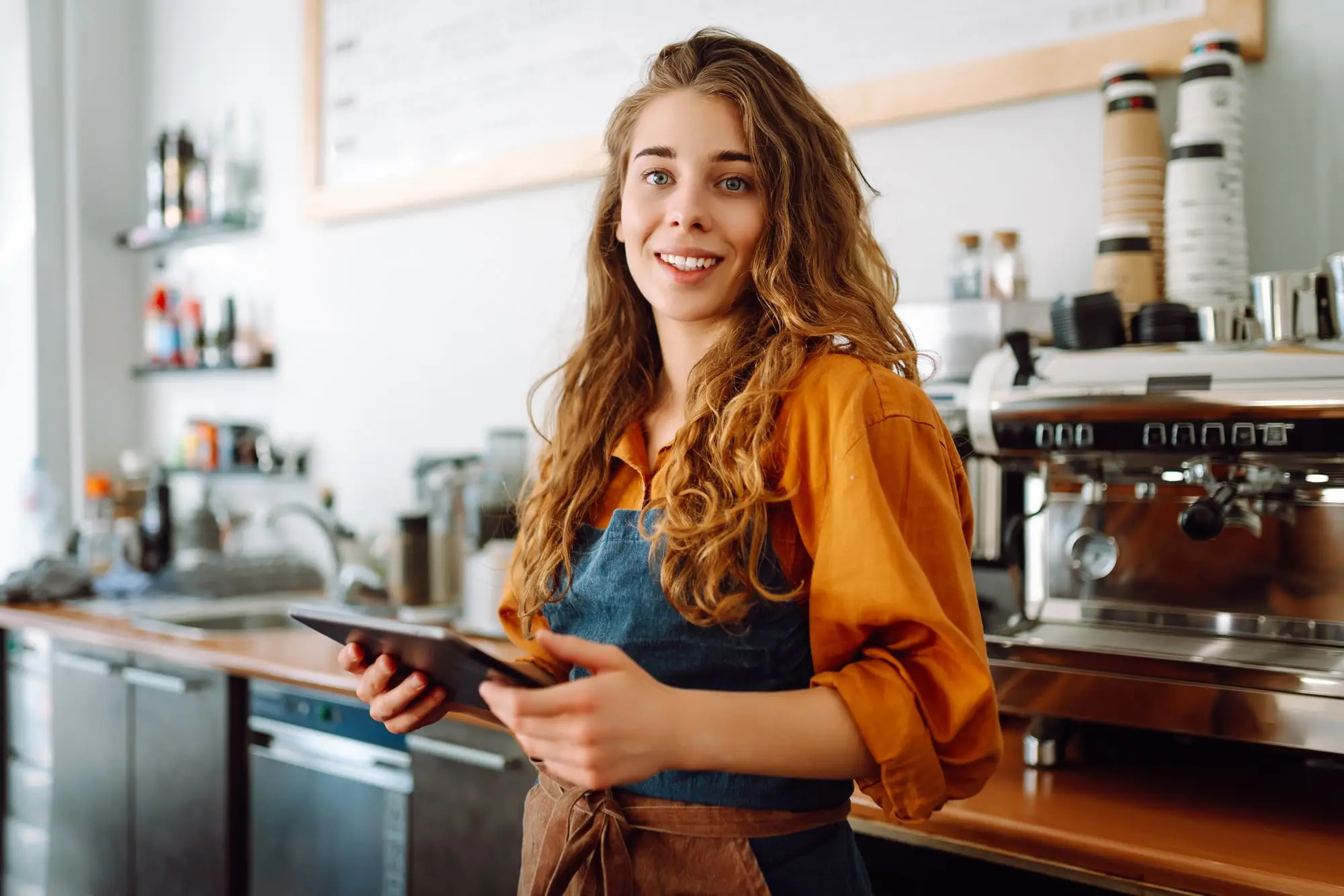 A café owner behind her counter holding a tablet