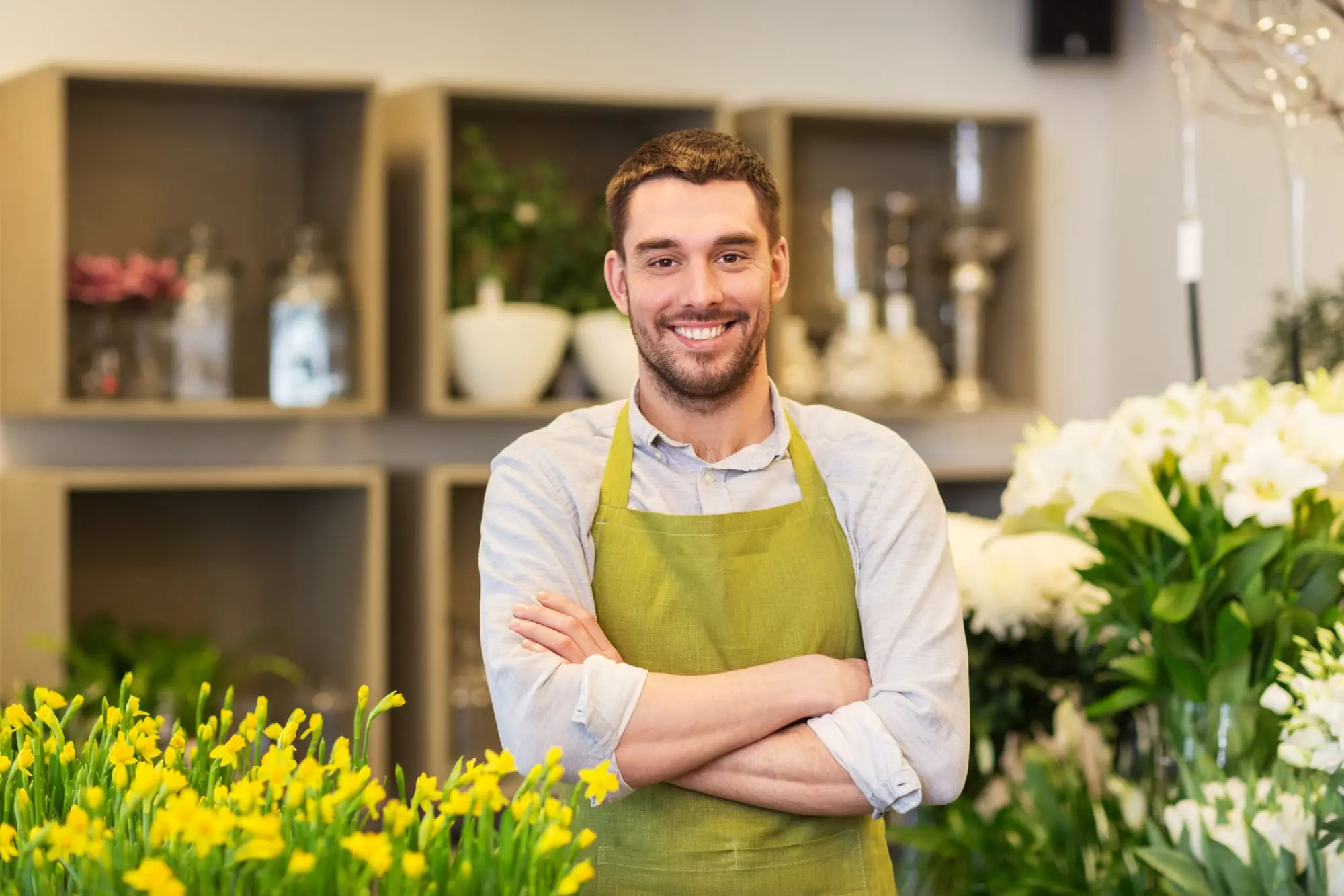 A florist standing in his flower shop, arms crossed and smiling