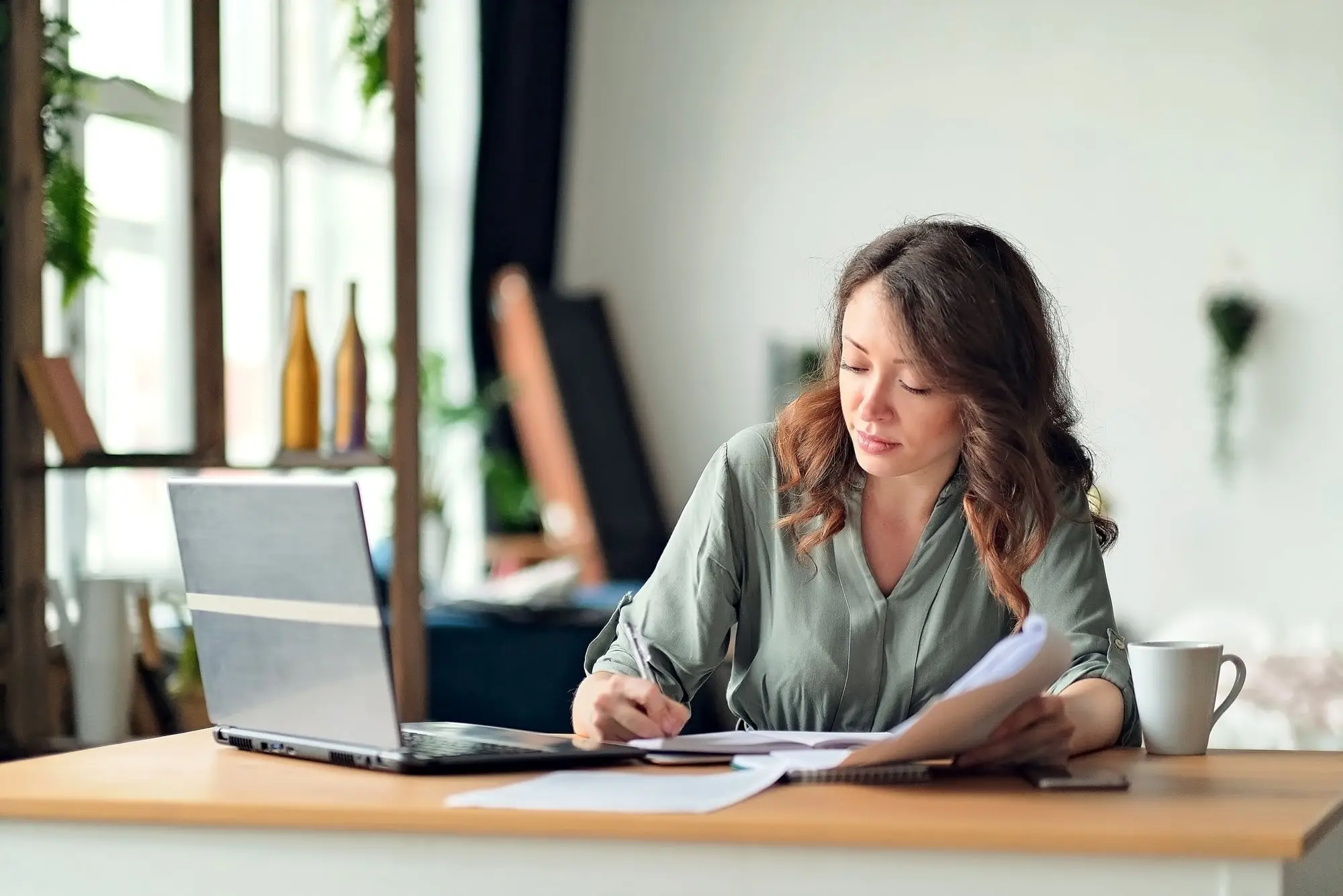 A freelancer working through paperwork at her desk at home, laptop open