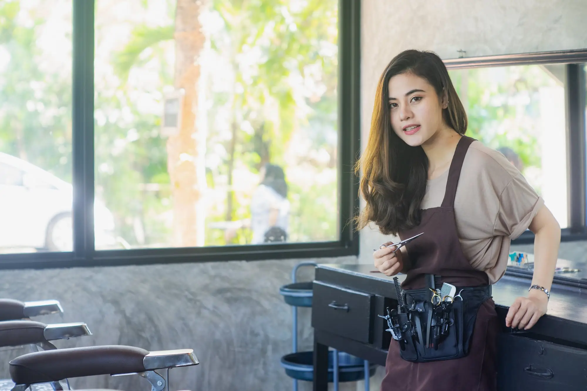 A hairdresser in her salon with her tools, leaning on the counter