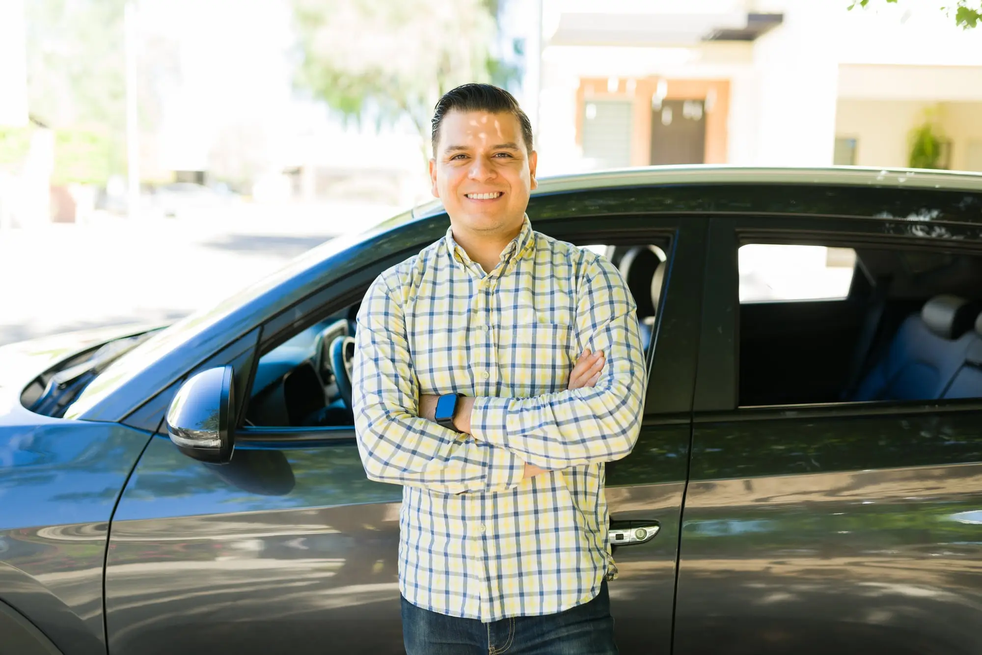 A rideshare driver standing beside his car, arms crossed